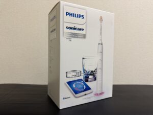 フィリップス ソニッケアー ダイヤモンドクリーンスマート HX9911のホワイト本体と充電グラスをダークな背景に並べたシネマティックな構図。34歳工場作業員が3ヶ月使った電動歯ブラシレビュー記事のアイキャッチ。